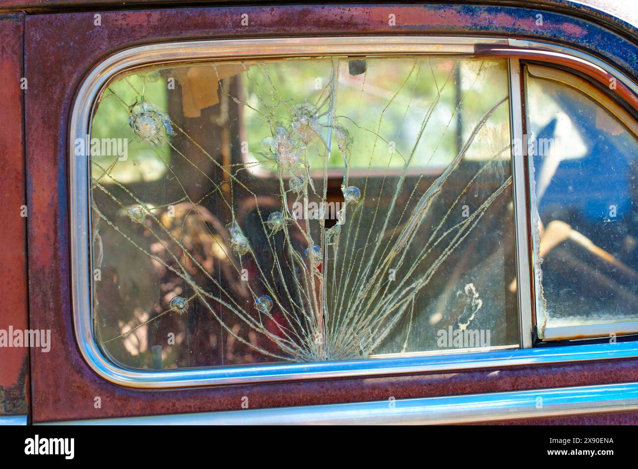Close-up view of a vintage car’s side window that has been shattered and covered with multiple radial cracks emanating from several impact points. Stock Photo
