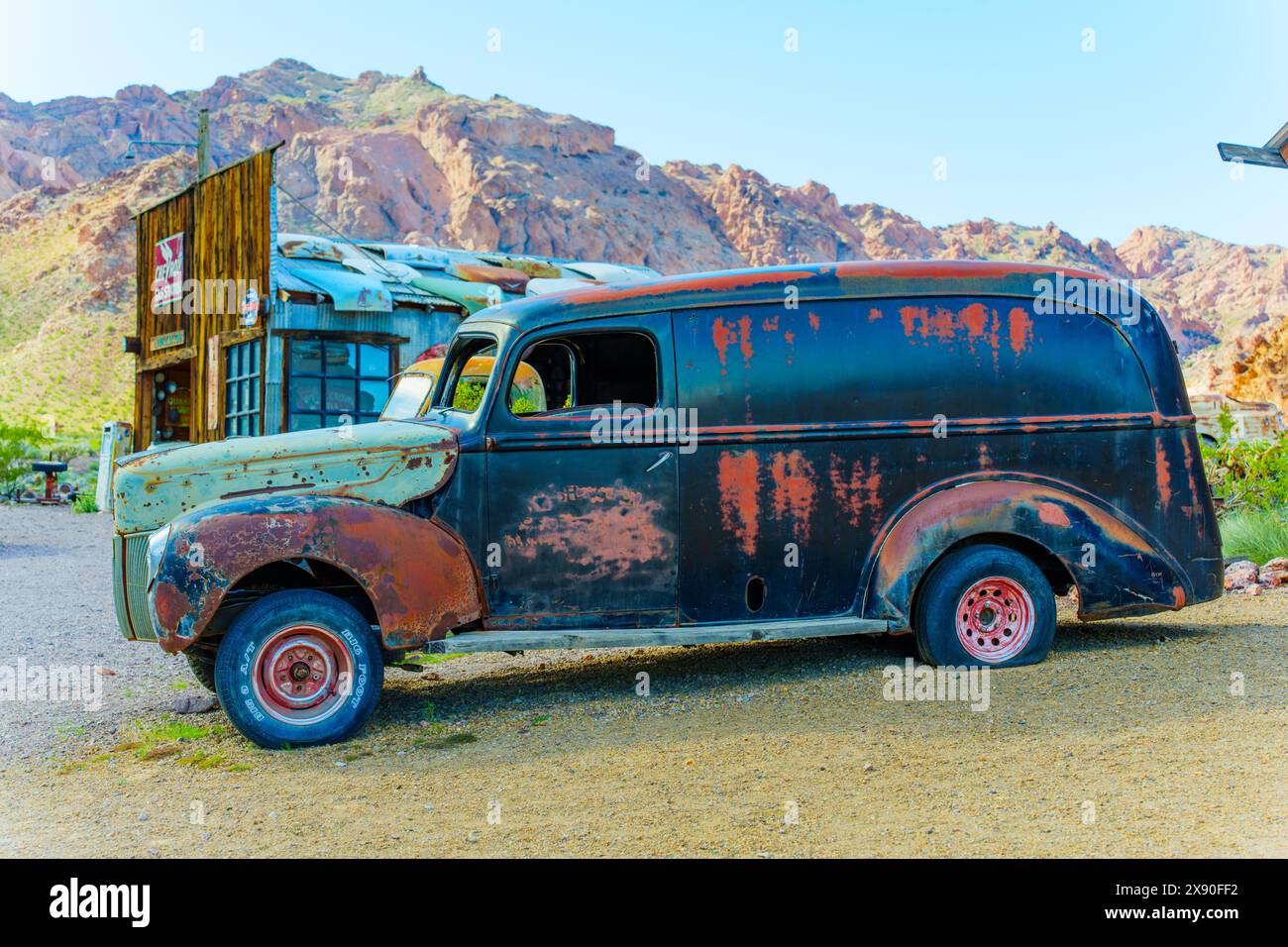 Nelson, Nevada - April 15, 2024: Close-up view of a corroded vintage car with an old body shop and mountains in the background Stock Photo