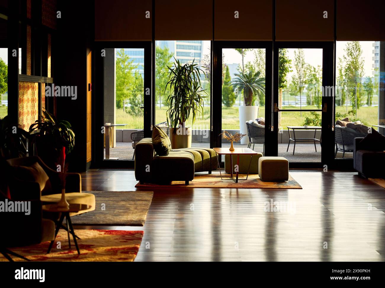 Modern hotel luxury lobby with panoramic window small wooden modern table, planter with green bushes and cozy sofa with reflection on the floor. Stock Photo