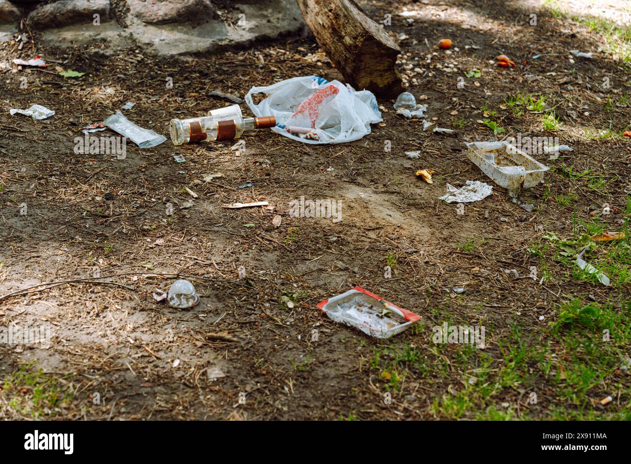 A lot of garbage, plastic bags, food packaging, glass bottles and other things are scattered in a picnic clearing in the forest. Stock Photo