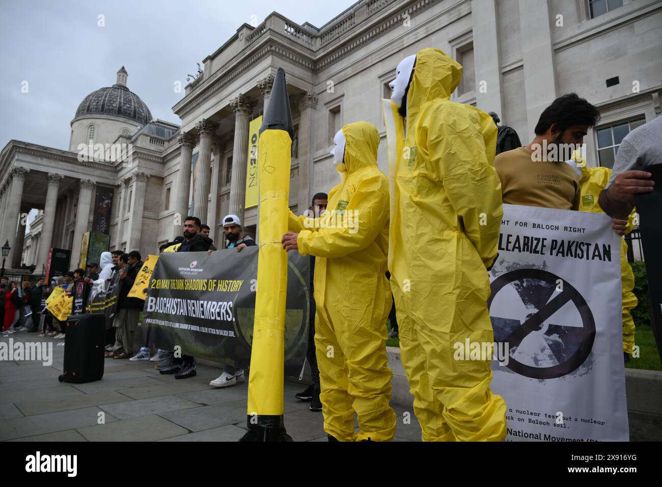 London, England, UK. 28th May, 2024. 25 years after five nuclear bombs were detonated underneath the Ras Koh Hills in Balochistan, activists with the group, Baloch National Movement hold a protest in London. Protesters wearing nuclear protection equipment hold a makeshift nuclear rocket. (Credit Image: © Cal Ford/ZUMA Press Wire) EDITORIAL USAGE ONLY! Not for Commercial USAGE! Stock Photo