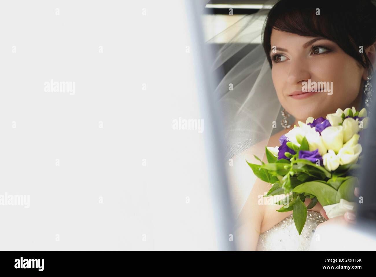 A smiling bride holding a bouquet of white and purple flowers, gazing serenely, Belarus, Minsk Stock Photo