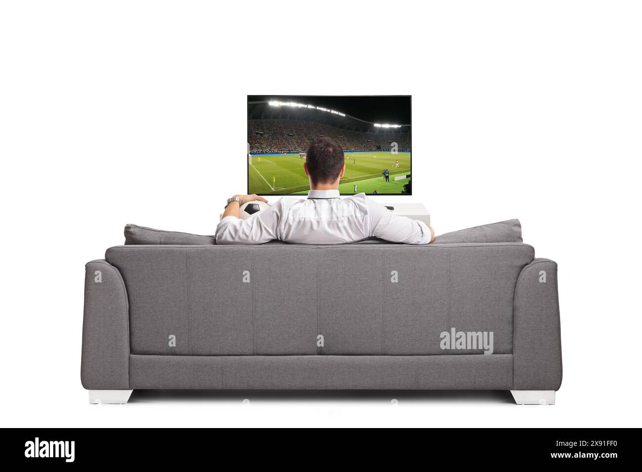 Man sitting on a sofa with a football and watching a match on tv ...