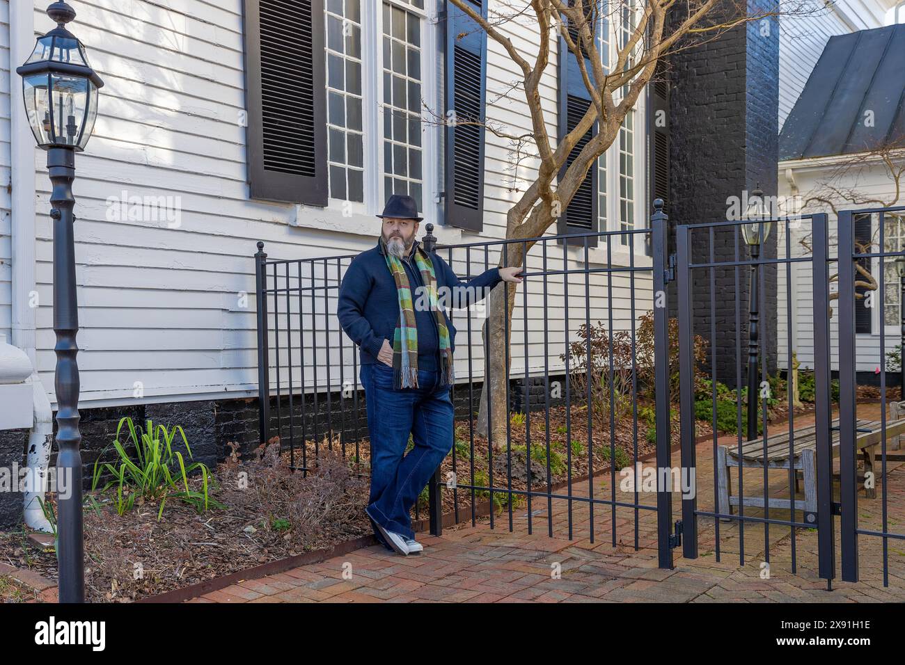 Wearing a hat and scarf a man stands in front of a garden courtyard gate in downtown Greenville, Tennessee, USA Stock Photo