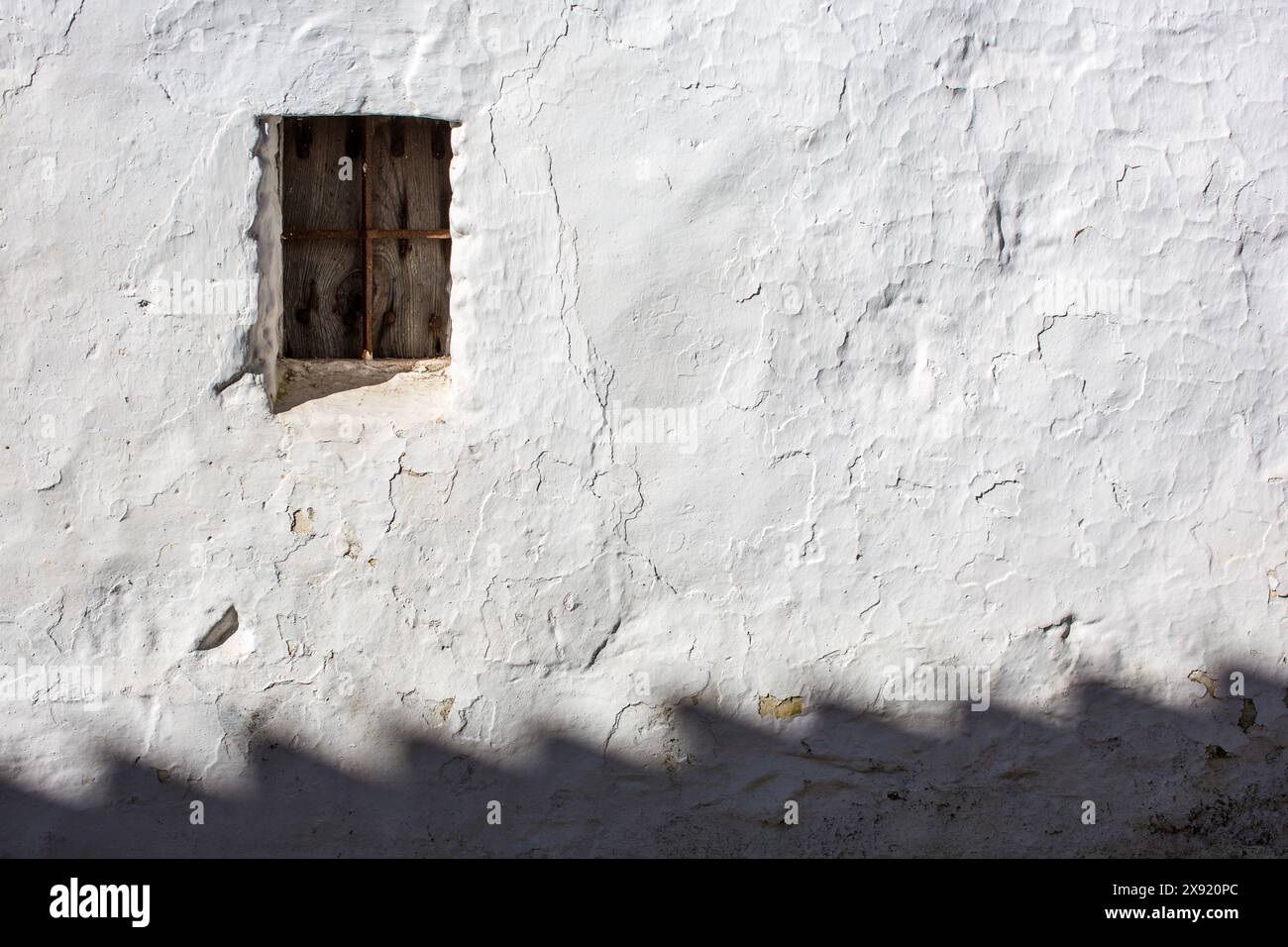 A small window set in a textured whitewashed wall, casting shadows in the afternoon sun. Stock Photo