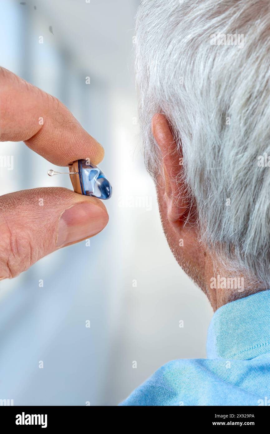 American shot of fitting a hearing aid to a white-haired senior citizen, rear view. Hearing aid for a senior man 016561 040 Stock Photo