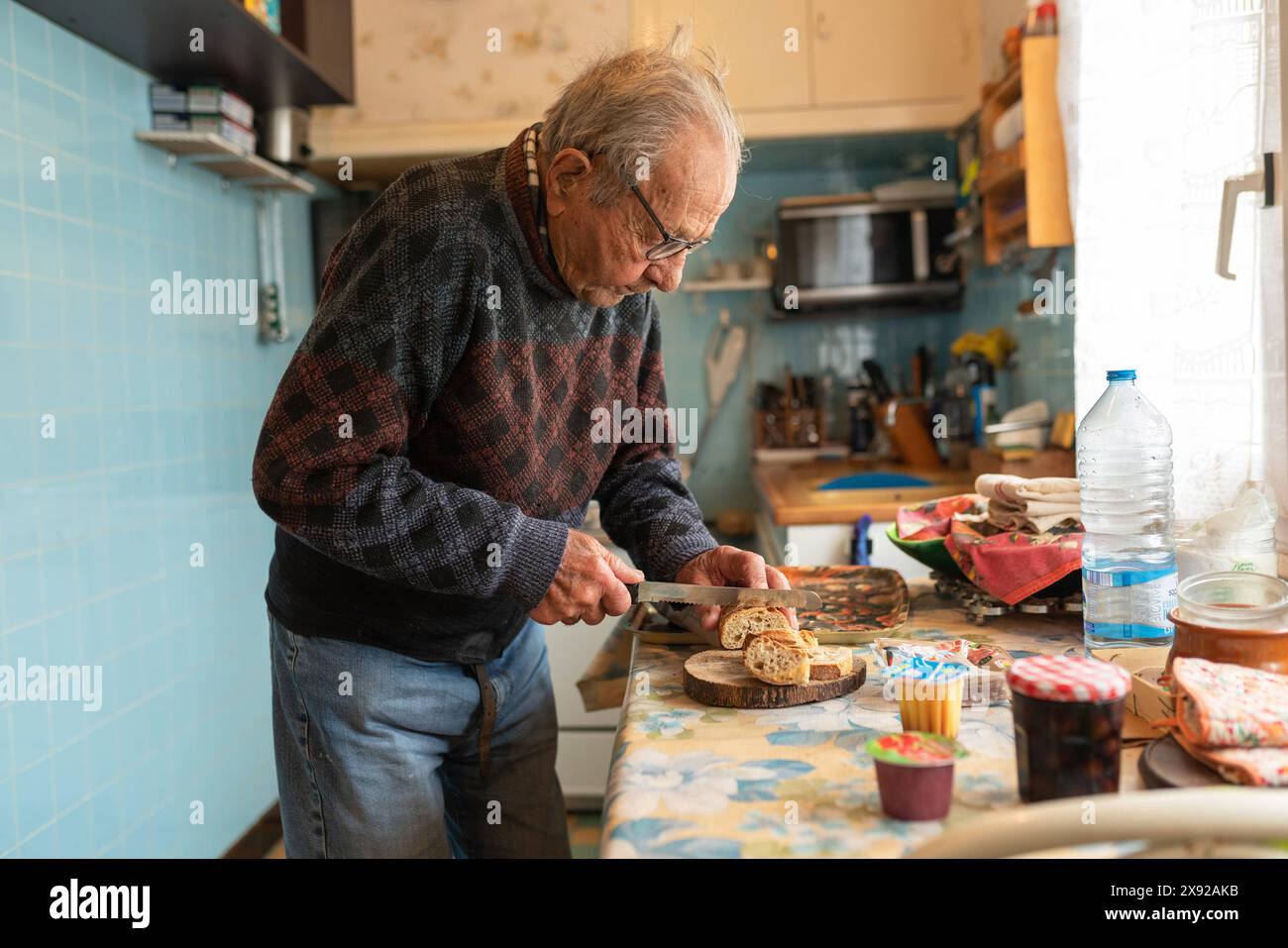 90 year old person cutting bread in his kitchen for his meal. 90 year old senior 016739 034 Stock Photo