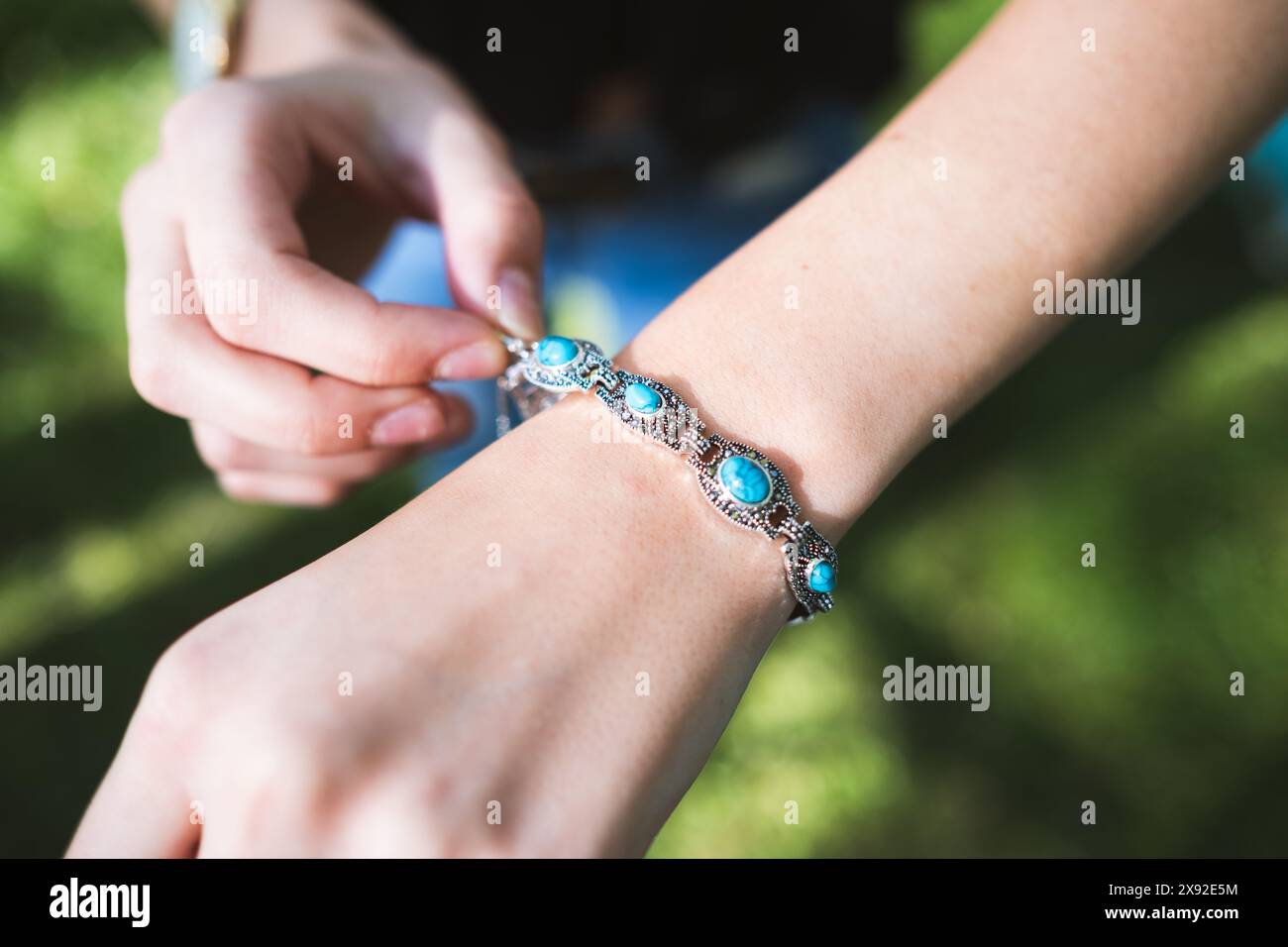 A young woman displays a silver and lapis lazuli bracelet in a natural outdoor setting Stock Photo