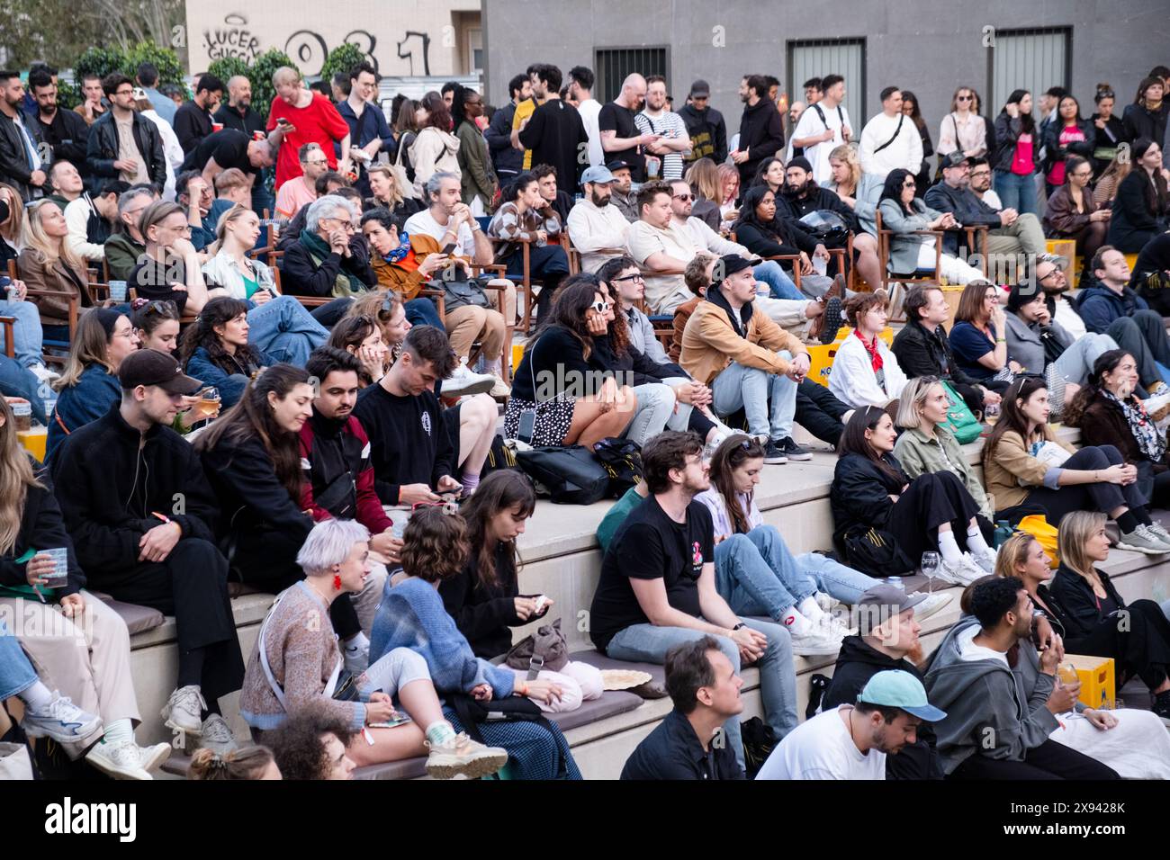 Attendees sit outside in the evening watching the talks from the main Roots Room on a large external screen at OFFF Barcelona at Disseny Hub Museum of Design in Barcelona, Spain in April 2024.  Picture: Rob Watkins.  INFO: The popular annual conference launched in 2001 and is the world's  largest showcase of contemporary visual creativity and design. It attracts designers, artists, filmmakers and photographers from around the world and serves as a global platform for creative exchange and collaboration. Stock Photo