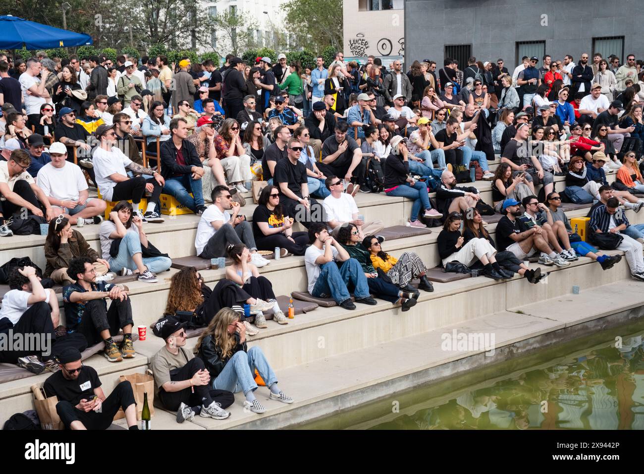 Attendees sit outside in the evening watching the talks from the main Roots Room on a large external screen at OFFF Barcelona at Disseny Hub Museum of Design in Barcelona, Spain in April 2024.  Picture: Rob Watkins.  INFO: The popular annual conference launched in 2001 and is the world's  largest showcase of contemporary visual creativity and design. It attracts designers, artists, filmmakers and photographers from around the world and serves as a global platform for creative exchange and collaboration. Stock Photo