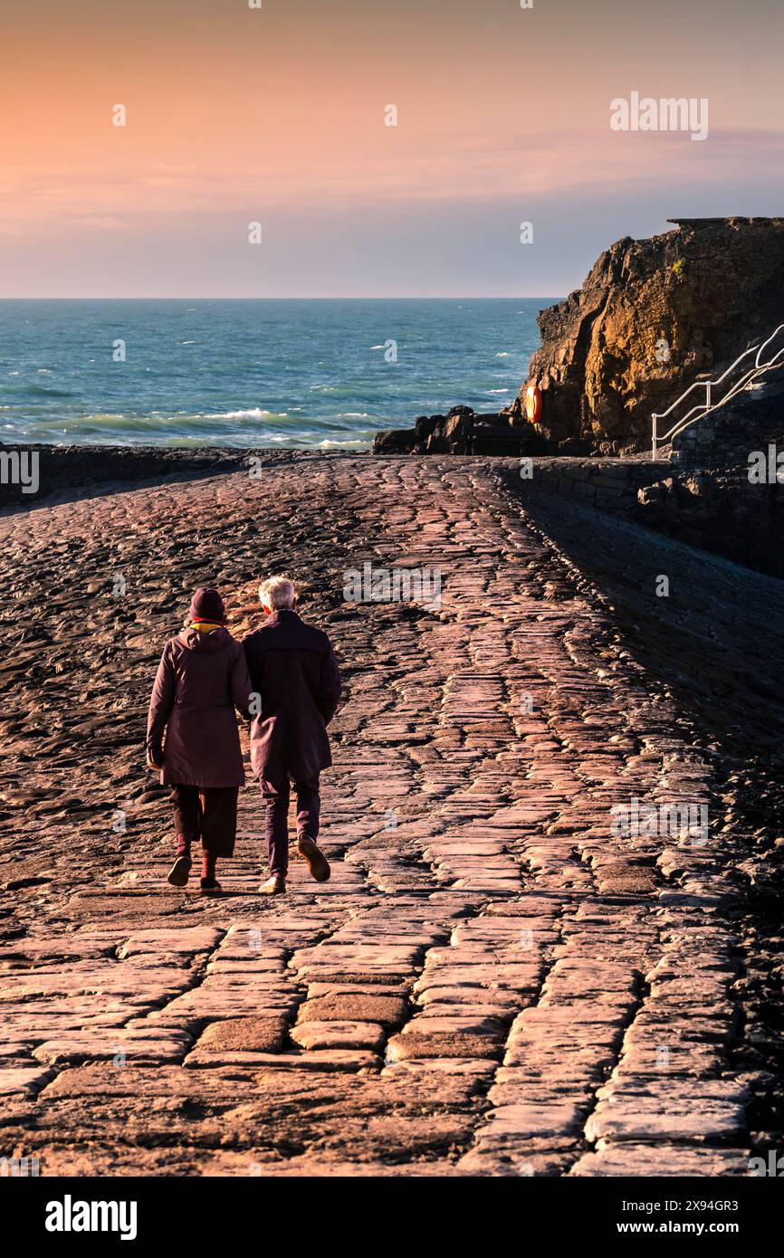 A mature couple walking along the breakwater levee in Bude in Cornwall in the UK. Stock Photo