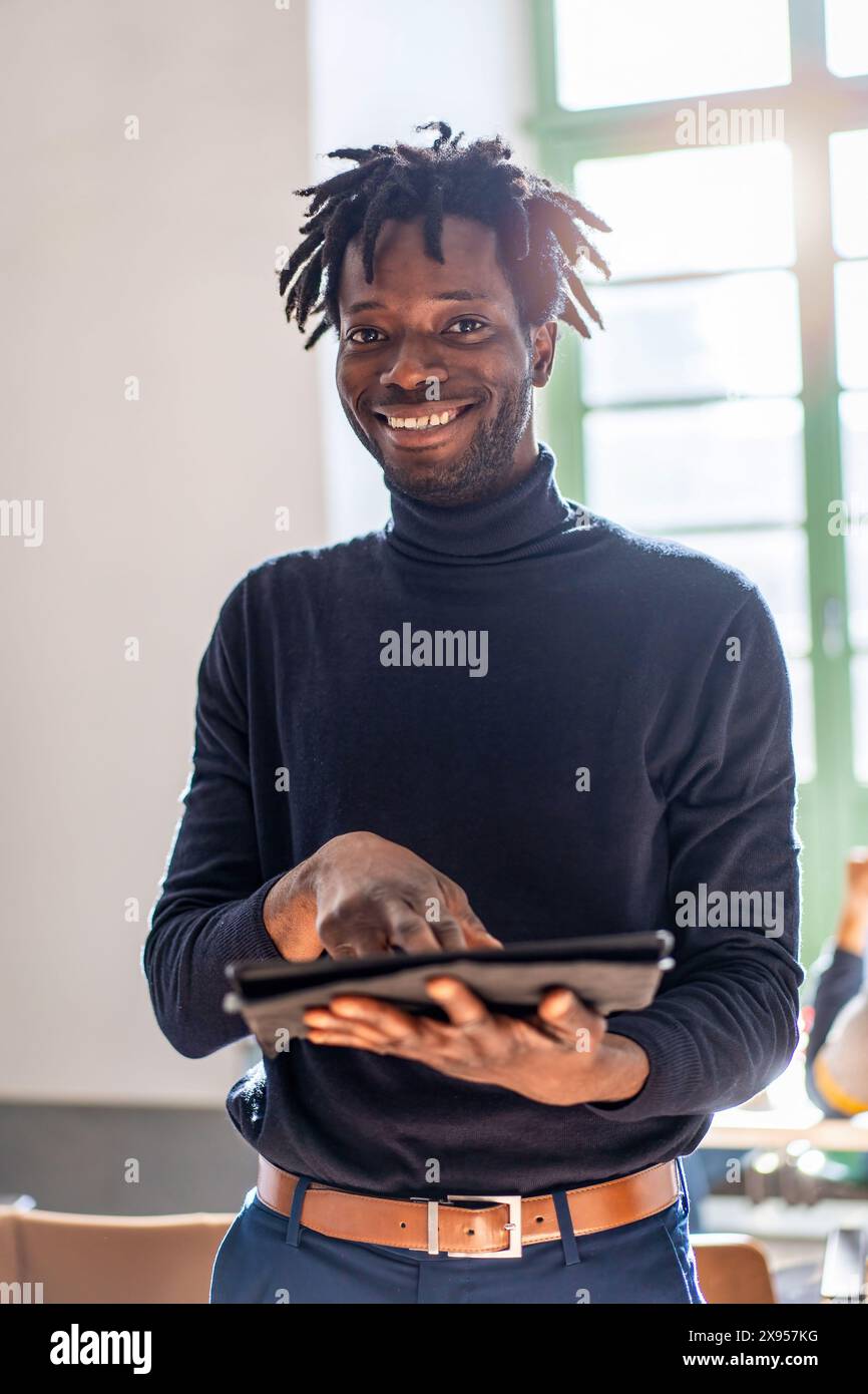 A smiling young African man using a digital tablet indoors. The image captures the essence of modern technology use, showcasing a cheerful, tech-savvy Stock Photo
