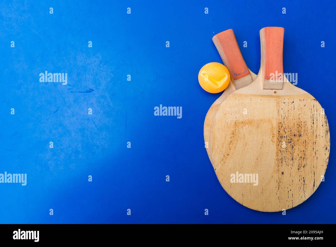 pair of old pingpong rackets and a dented ball on a blue pingpong table Stock Photo
