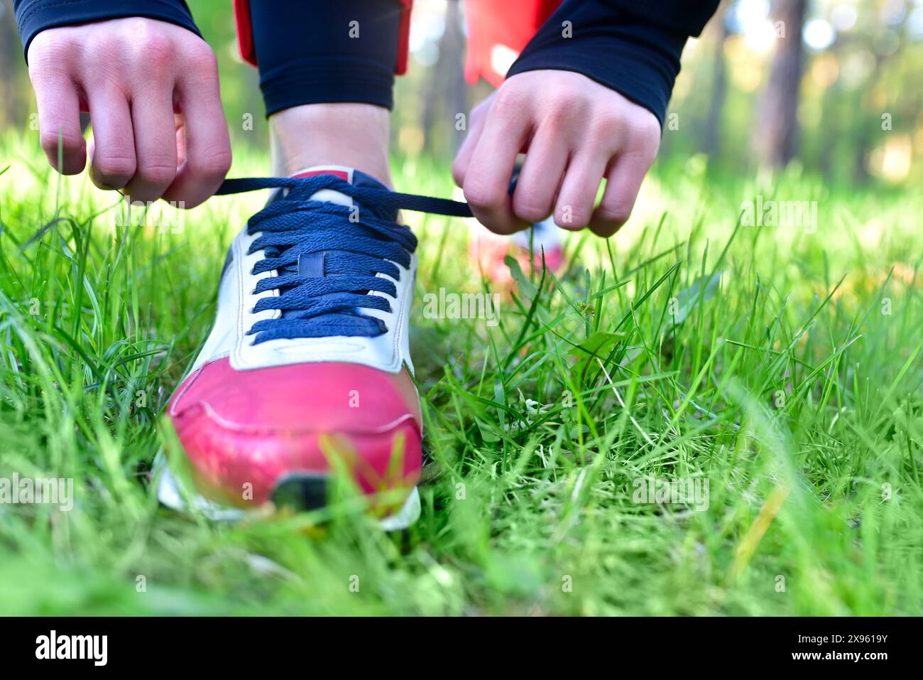 A woman tightens the laces on her athletic sneakers in a park while jogging Stock Photo