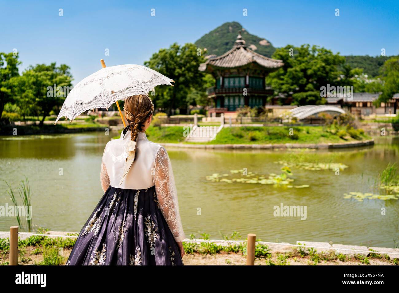 South Korea, Seoul. Woman in hanbok. Gyeongbokgung palace park garden. Hyangwonjeong Pavilion in the background. Korean dress tradition. Stock Photo