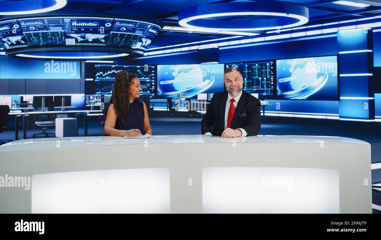 TV Live News Program: Two Professional Presenters Reporting On the Events. Television Cable Channel Newsroom Studio: Male and Female Anchors Talk. Mock-up Broadcasting Network Concept. Wide Shot Stock Photo