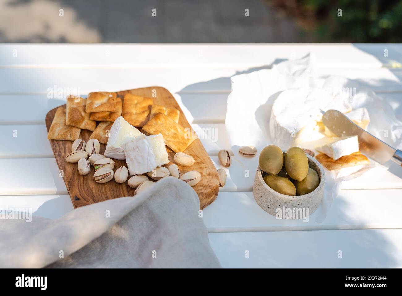 Wine appetizers namely pistachios, camembert cheese, saltine crackers and olives on a white table outdoors. Stock Photo