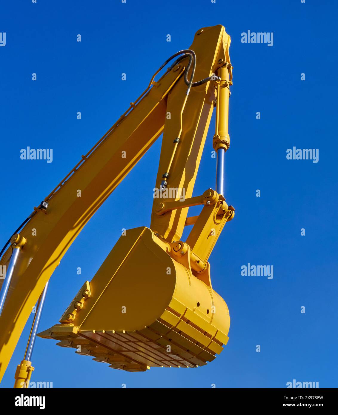 Scoop and hydraulic arm of an excavator, isolated on clear blue sky background, low angle perspective shot. Stock Photo