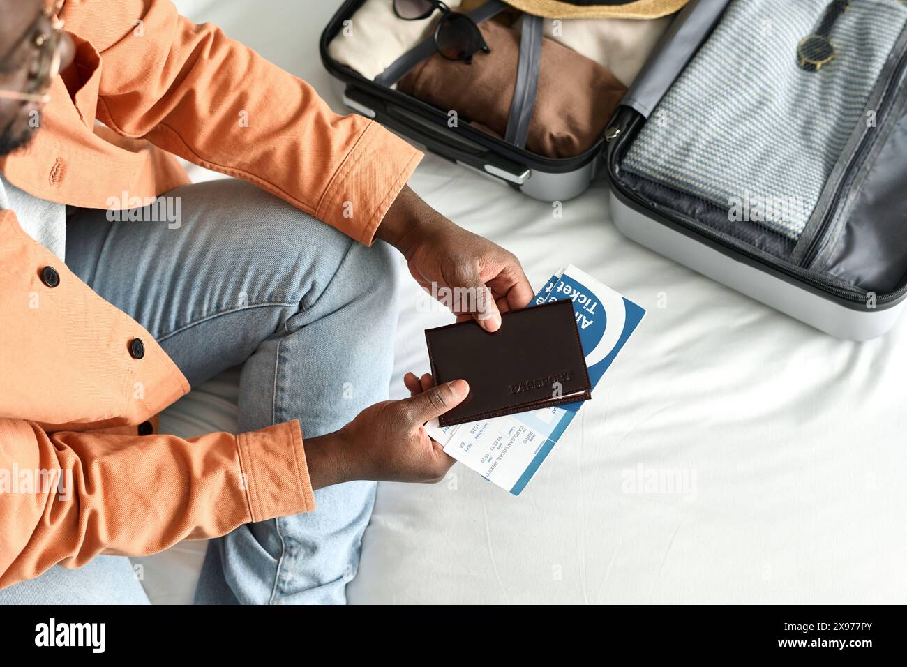 Top view close up of unrecognizable Black man holding passport and tickets sitting on bed in hotel room and preparing for travel copy space Stock Photo