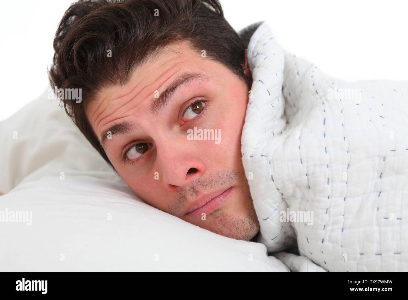 close up of a young man in bed under blanket with discontent face Stock Photo