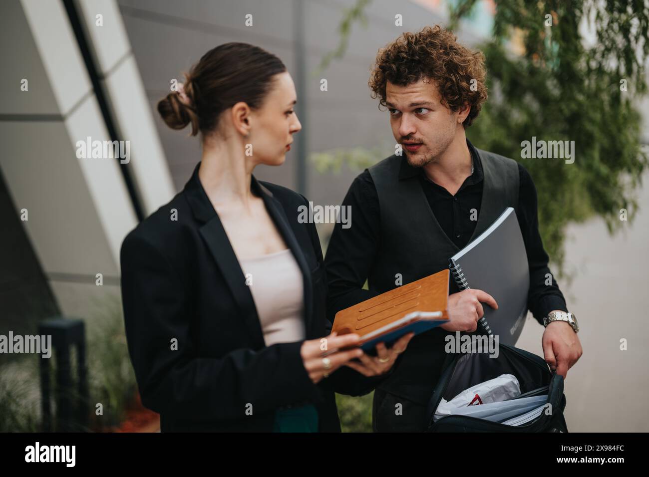 Two business professionals having an outdoor discussion while exchanging notebooks Stock Photo