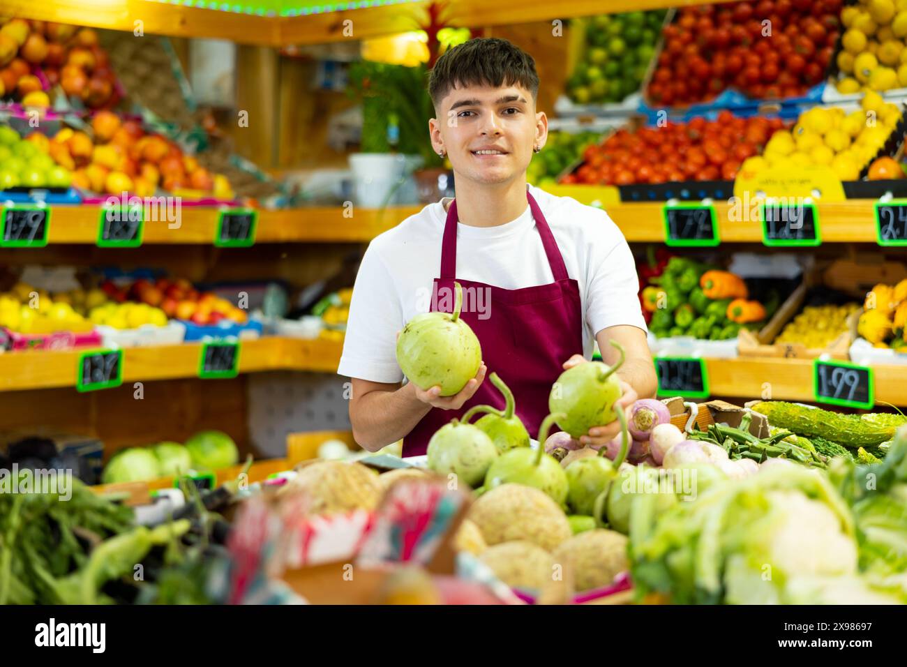 Young salesman working and posing in store near counter with round bottlegourd vegetable Stock Photo