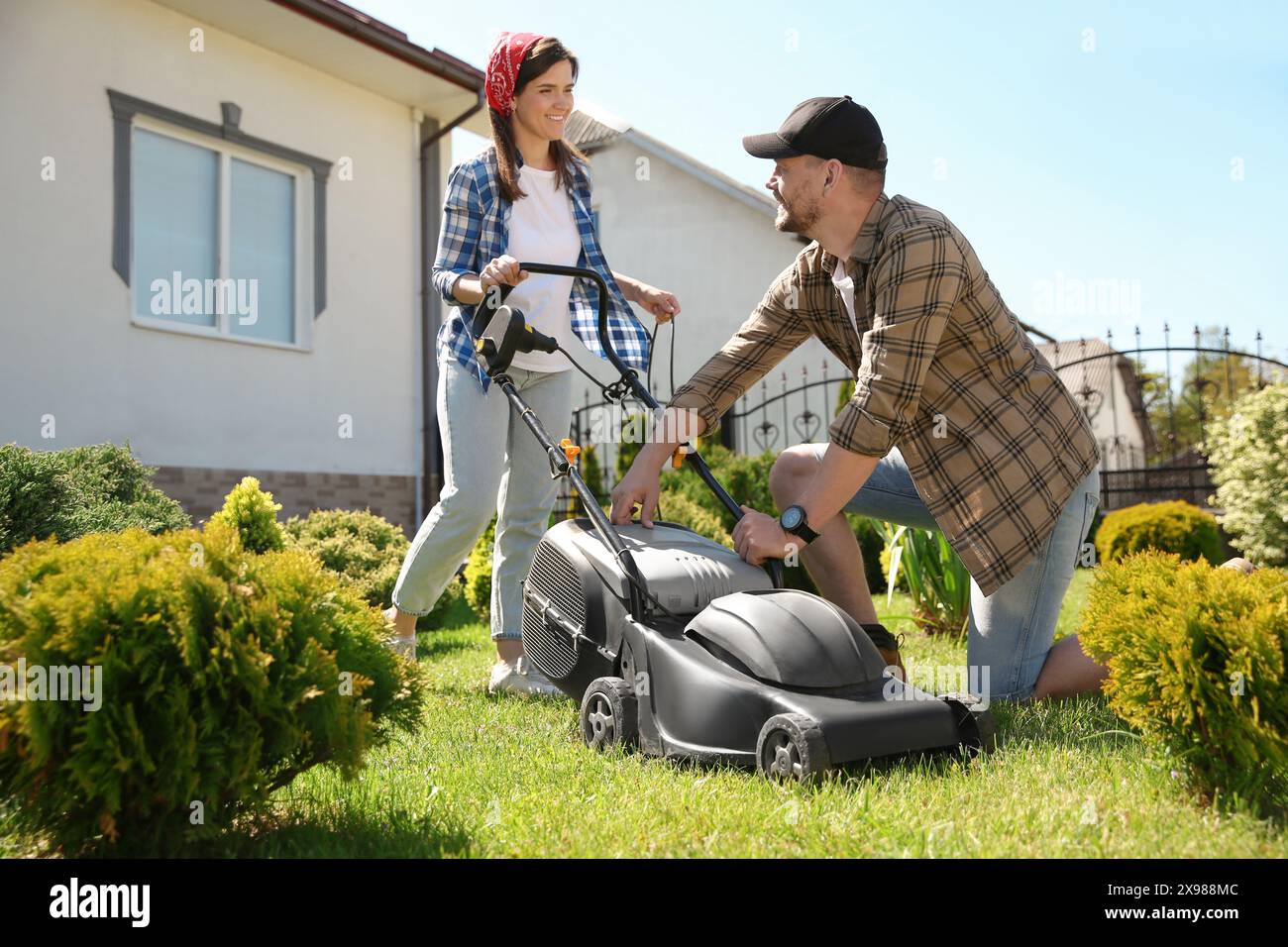 Happy couple spending time together while cutting green grass with lawn ...