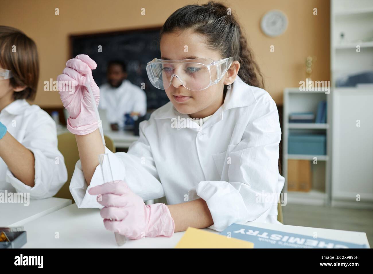Middle Eastern girl wearing lab coat and goggles sitting at table in ...