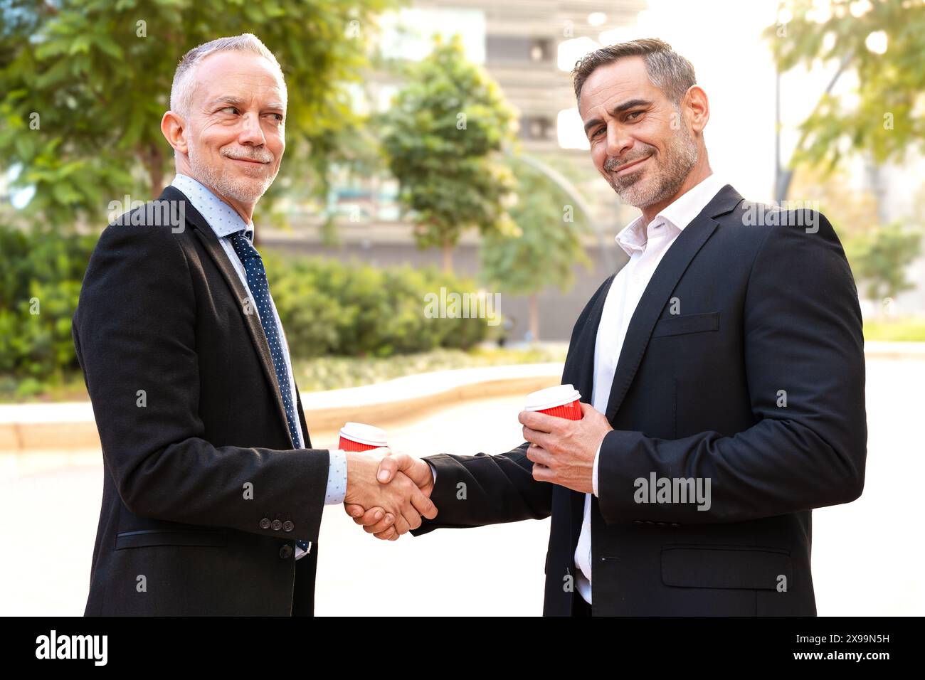 Two successful businessmen standing shaking hands, looking at the camera. Stock Photo