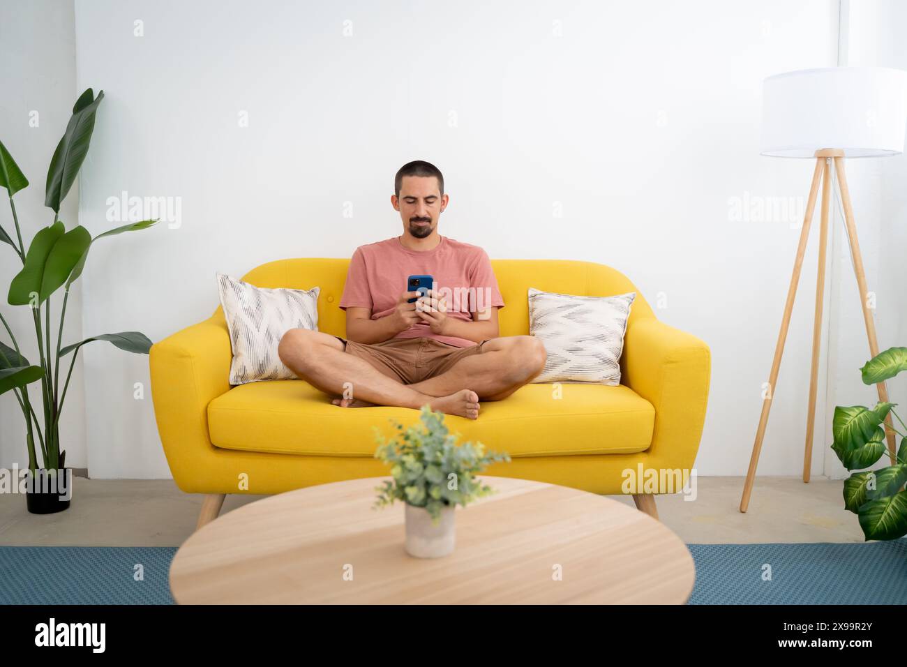 Smiling young man with smartphone sitting on sofa at home Stock Photo