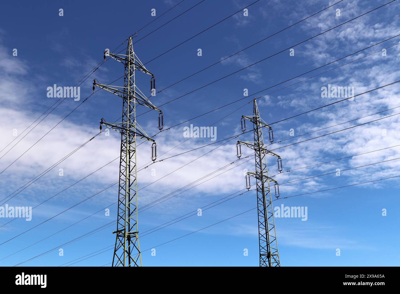 High voltage power pylons standing against a blue sky with white clouds ...