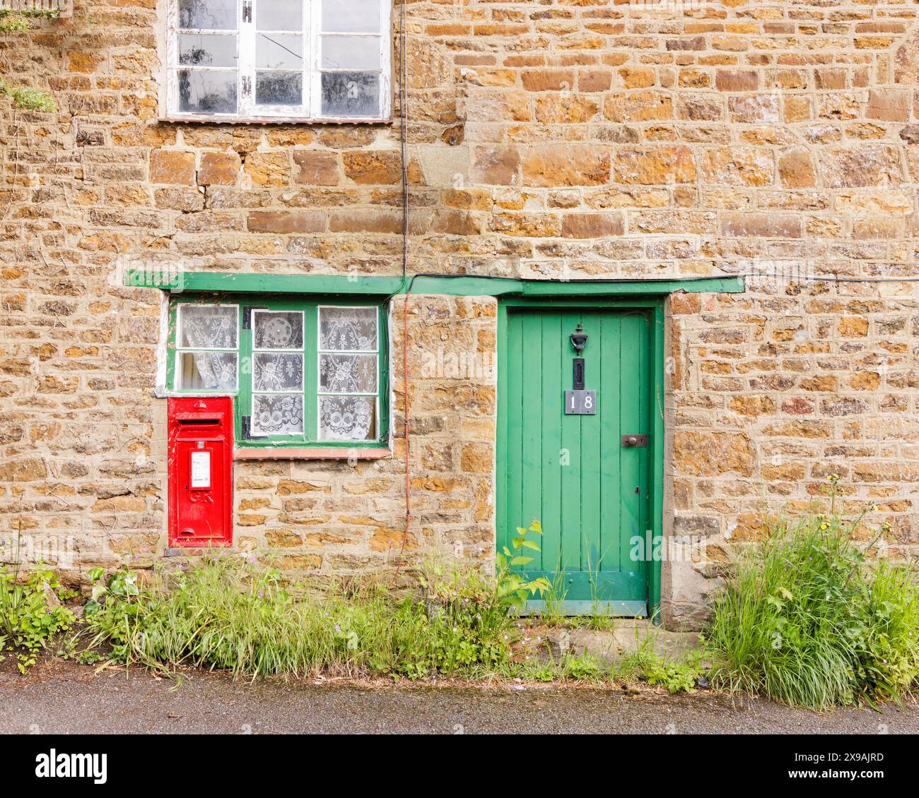 Charwelton, Northamptonshire, UK - May 2024: A built-in post box in the Northamptonshire stone wall of a cottage with a green door and windowframe. Stock Photo