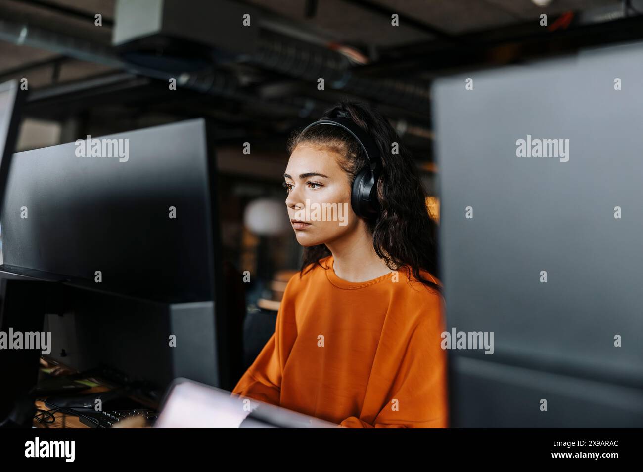 Focused female computer programmer with wireless headphones working at office Stock Photo
