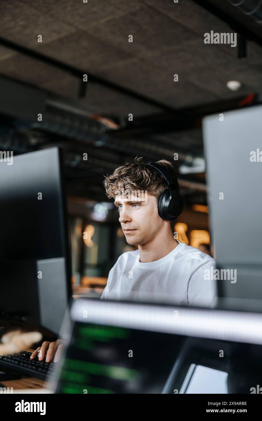Young male programmer doing coding on computer while sitting at tech start up office Stock Photo