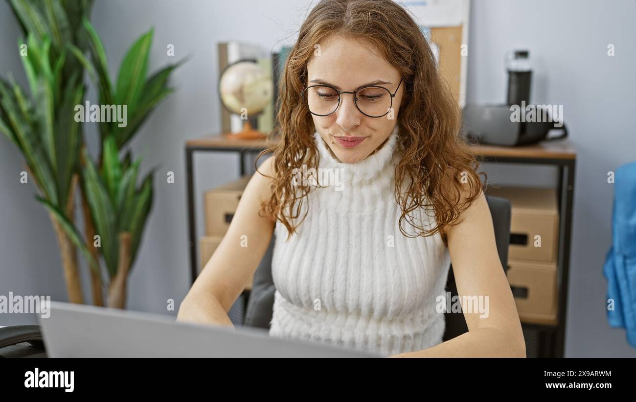 A young woman works attentively at her laptop in a modern office ...