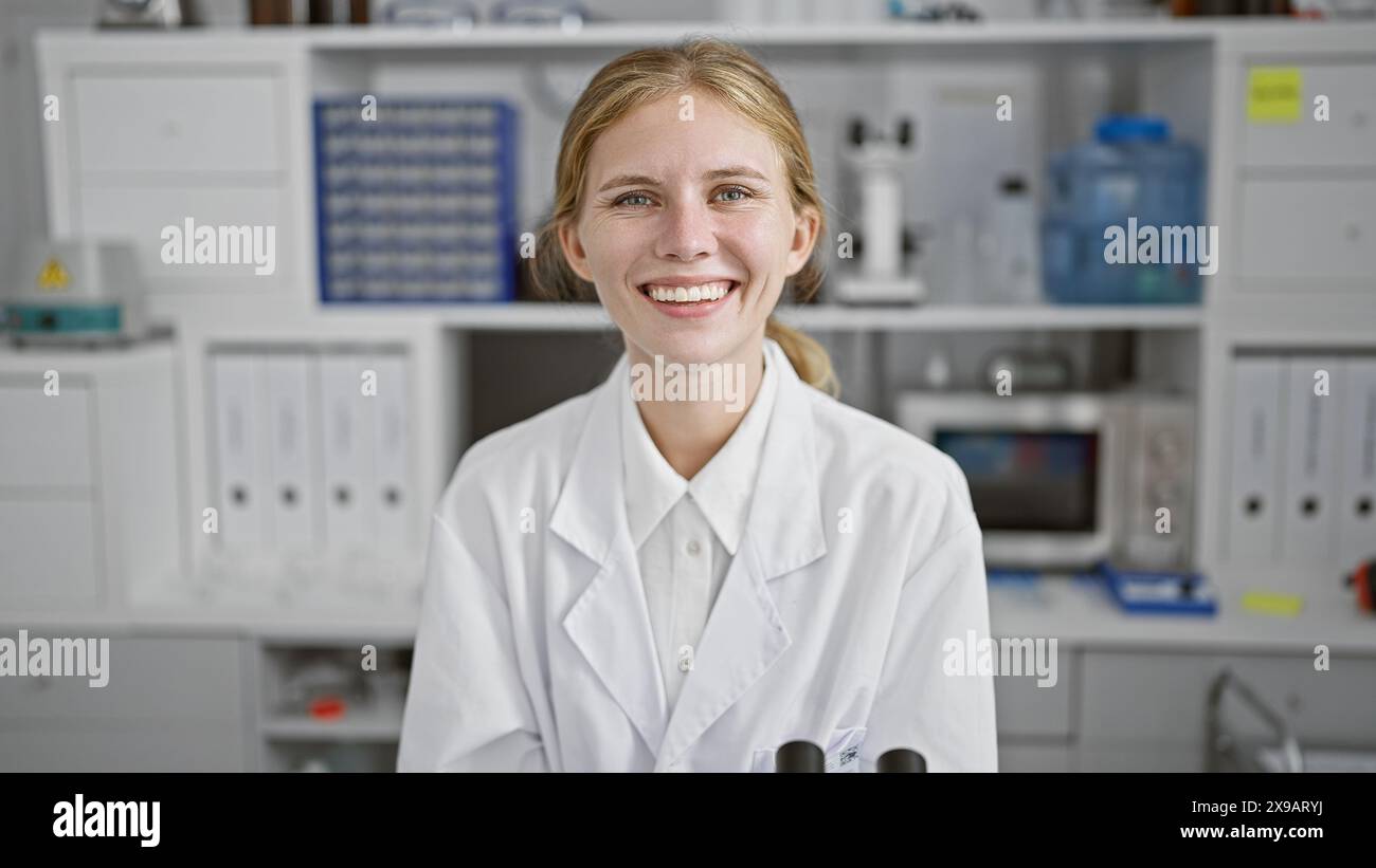 Smiling young woman in white lab coat standing in a medical laboratory ...