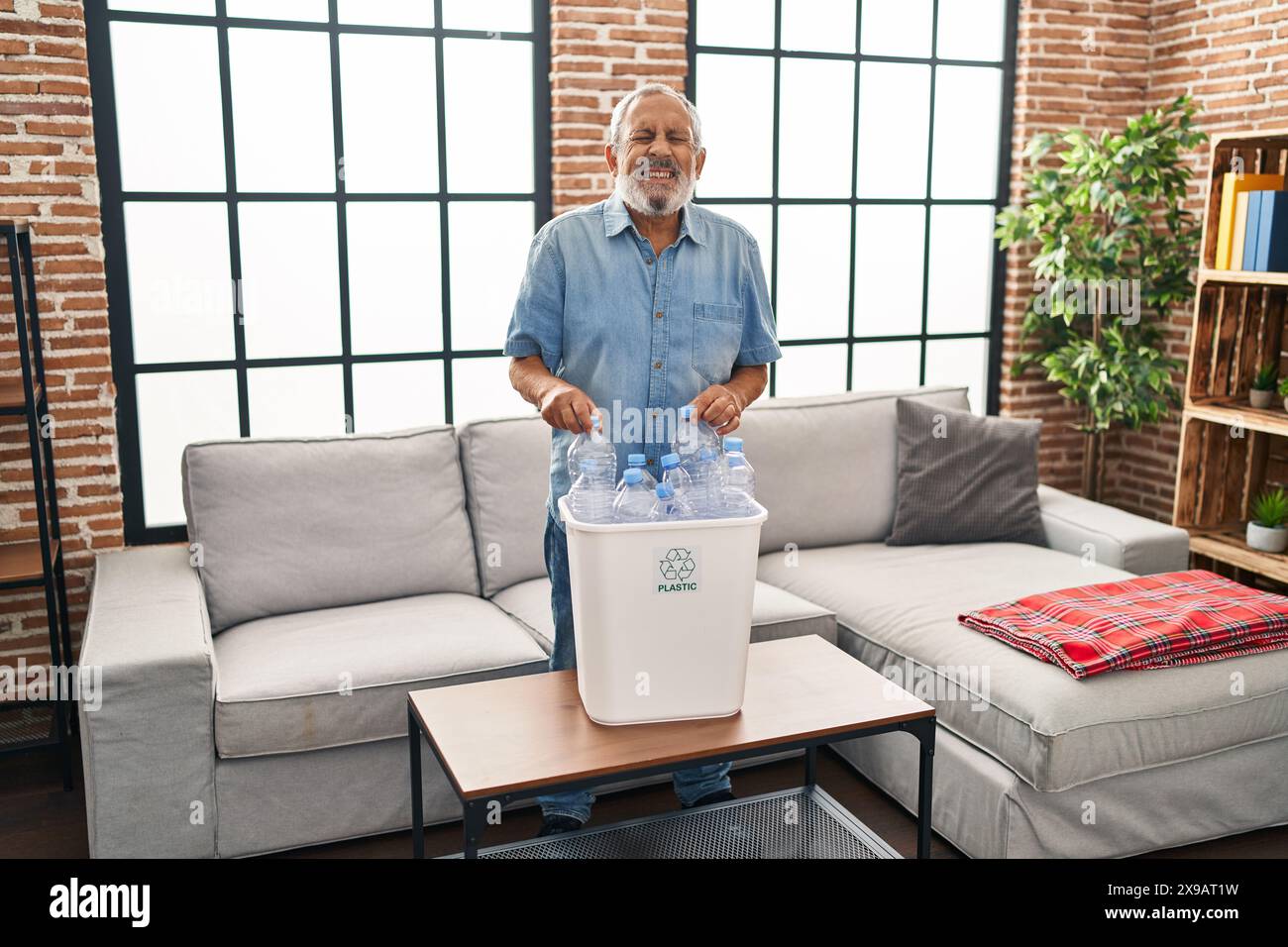 Cheerful senior man having a laugh-out-loud moment recycling plastic bottles at home, spreading joy with a funny joke Stock Photo