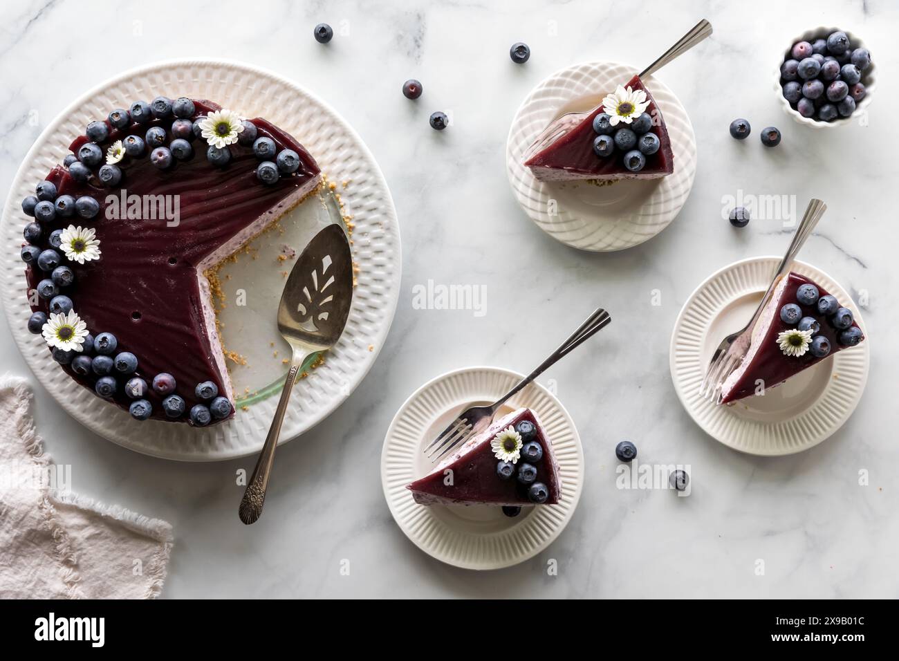 A blueberry cheesecake with serving slices to the side, ready for eating. Stock Photo