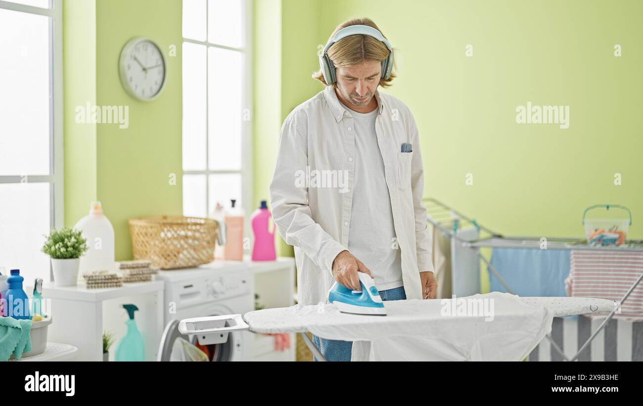 Handsome young man ironing clothes in a bright laundry room while ...