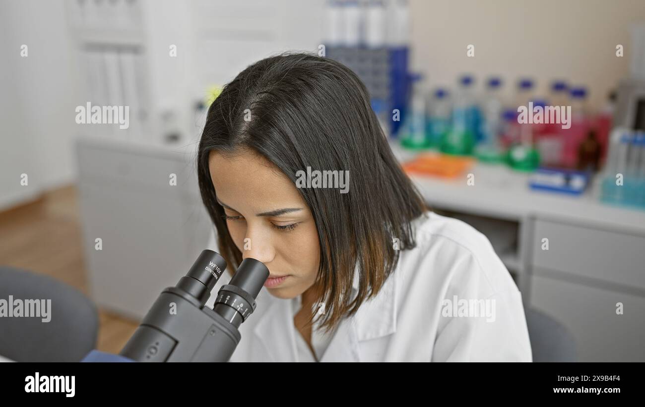 Concentrated young woman scientist using microscope in a modern laboratory setting. Stock Photo