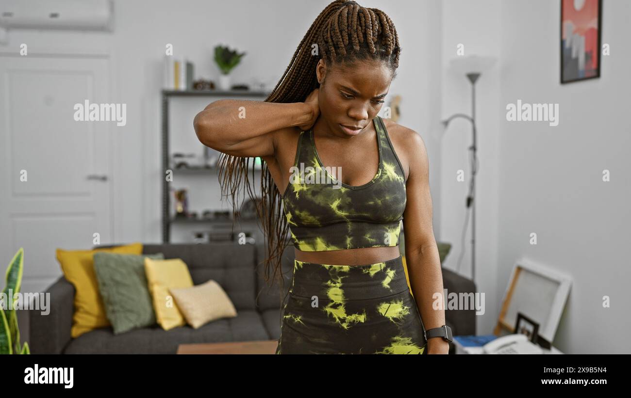 A black woman with braids feeling neck pain in a modern living room ...