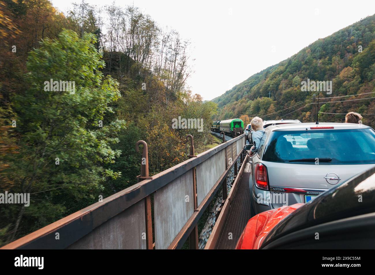 Young boys lean out a car window as it travels on the back of a motorail train carriage as it travels through tunnels and gorges in Slovenia Stock Photo