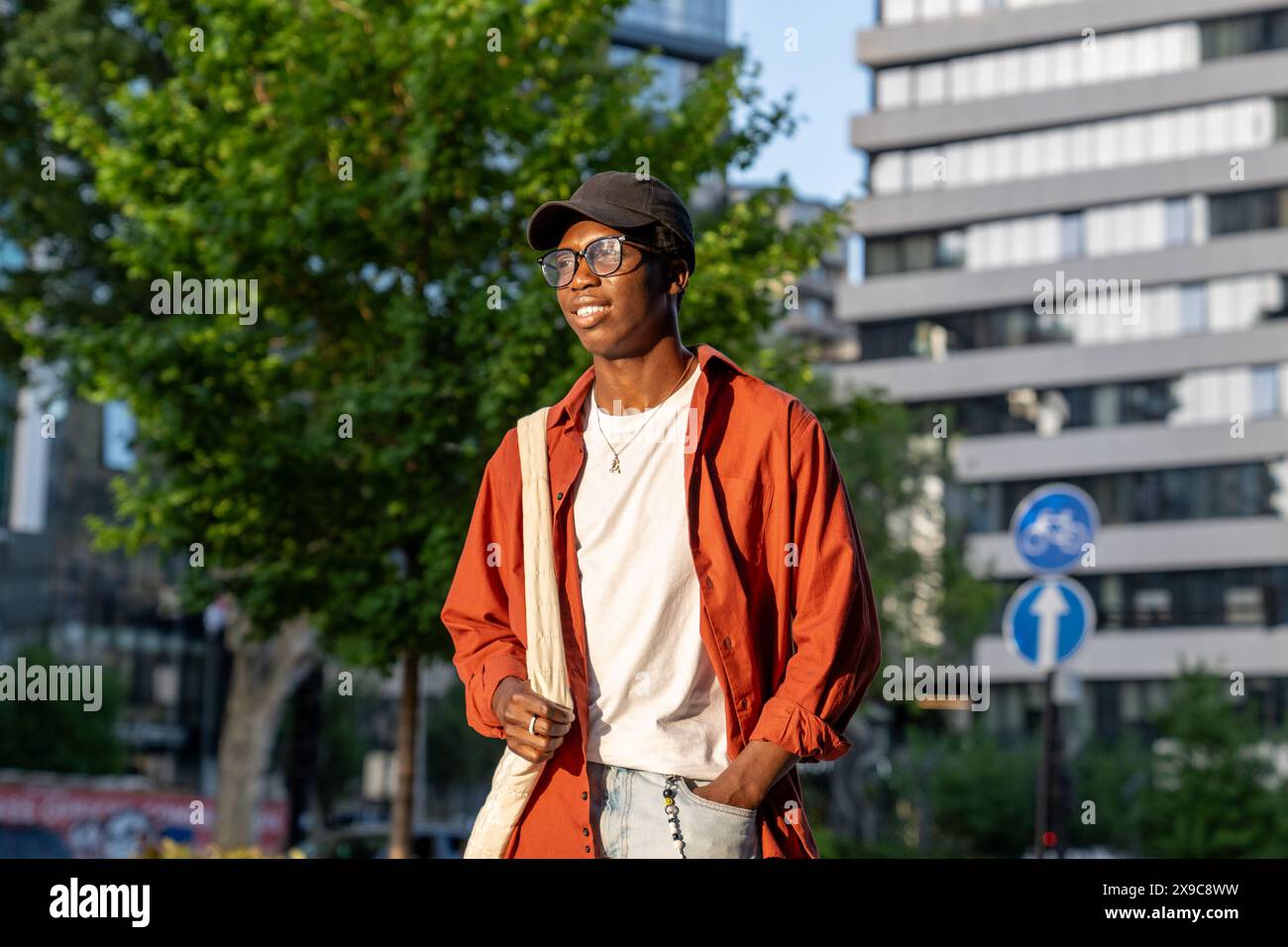 Confident stylish guy in glasses standing in city waits for friend for walking smiling looking away Stock Photo