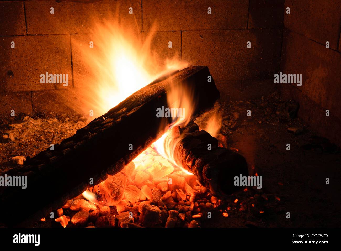 A close-up of a burning log in a fireplace, with flames and embers ...