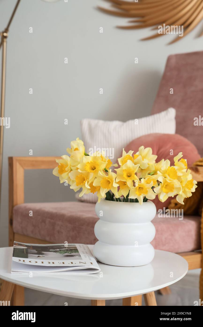 Armchair and coffee table with vase of narcissus flowers and magazine ...