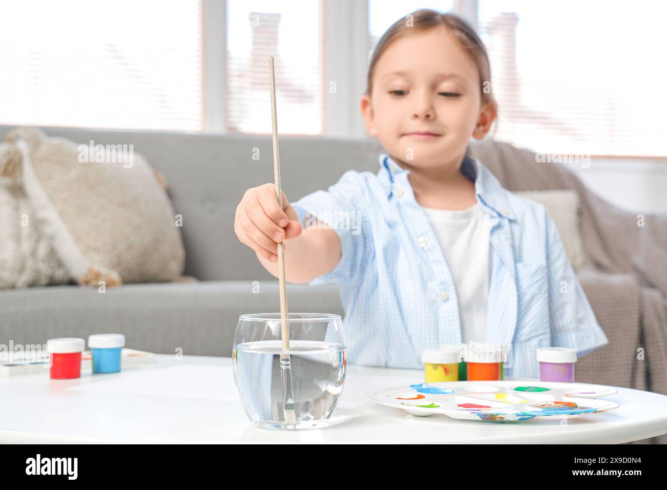 Cute little girl soaking paint brush in water at home, closeup Stock