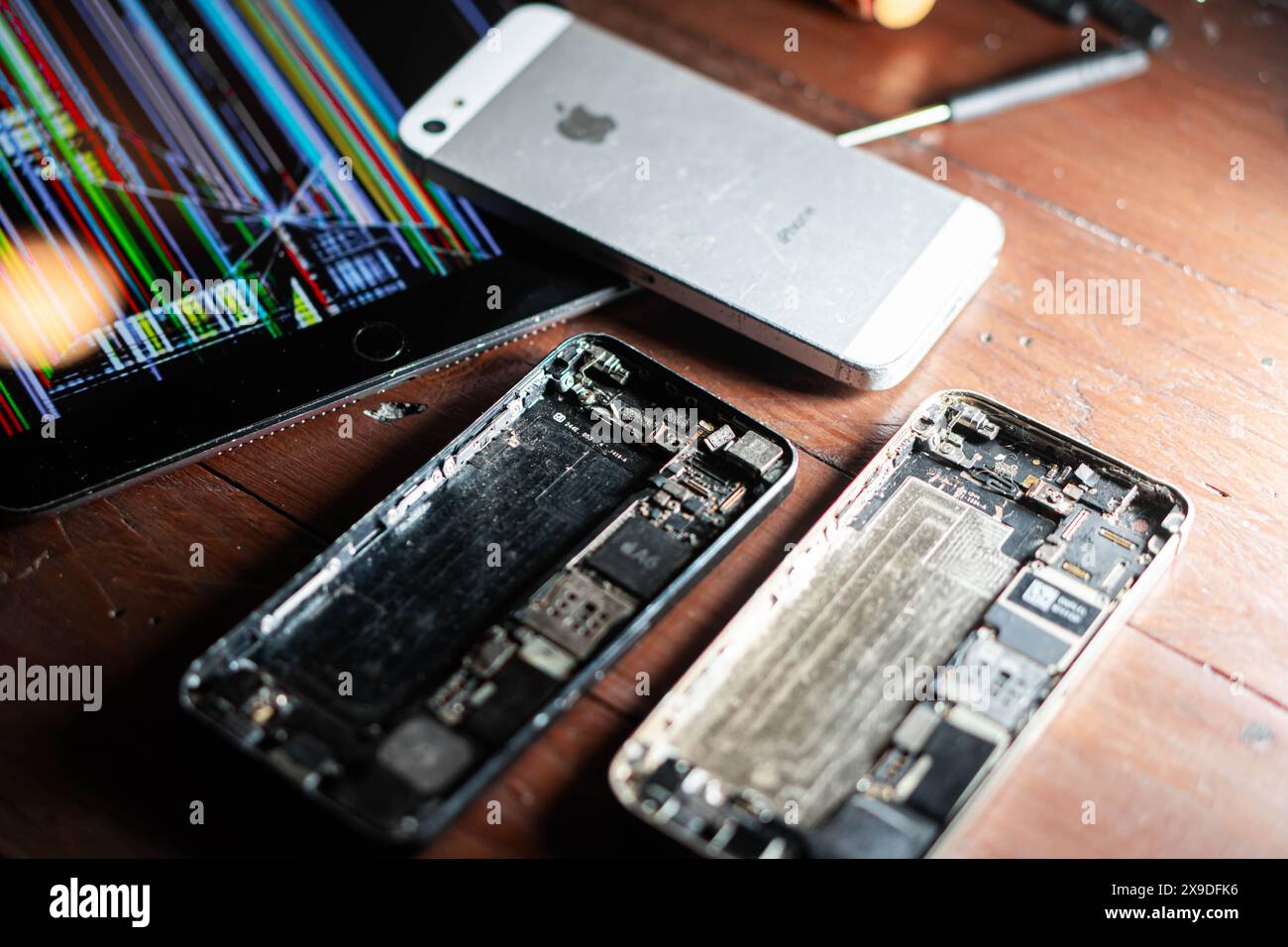 A disassembled smartphone with its internal components exposed, placed on a wooden surface. Nearby, a damaged tablet with a colorful striped screen an Stock Photo