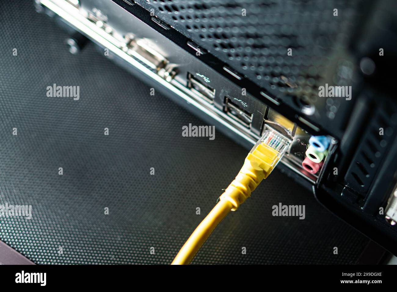 Close-up of a yellow Ethernet cable plugged into the back of a computer. The image shows the network port and other peripheral ports on the computer. Stock Photo