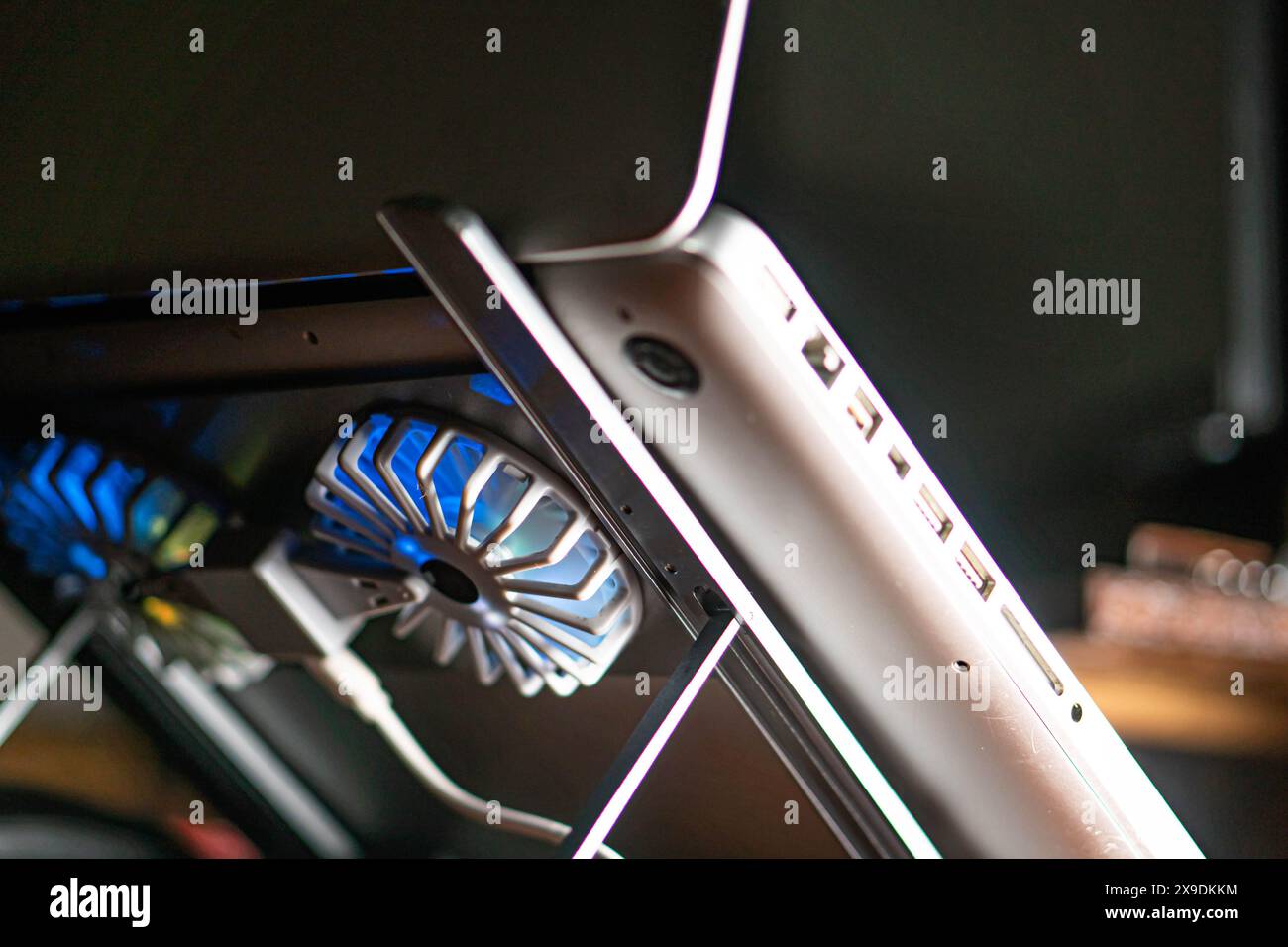 A close-up of a laptop on a cooling stand with blue LED fans. The ...