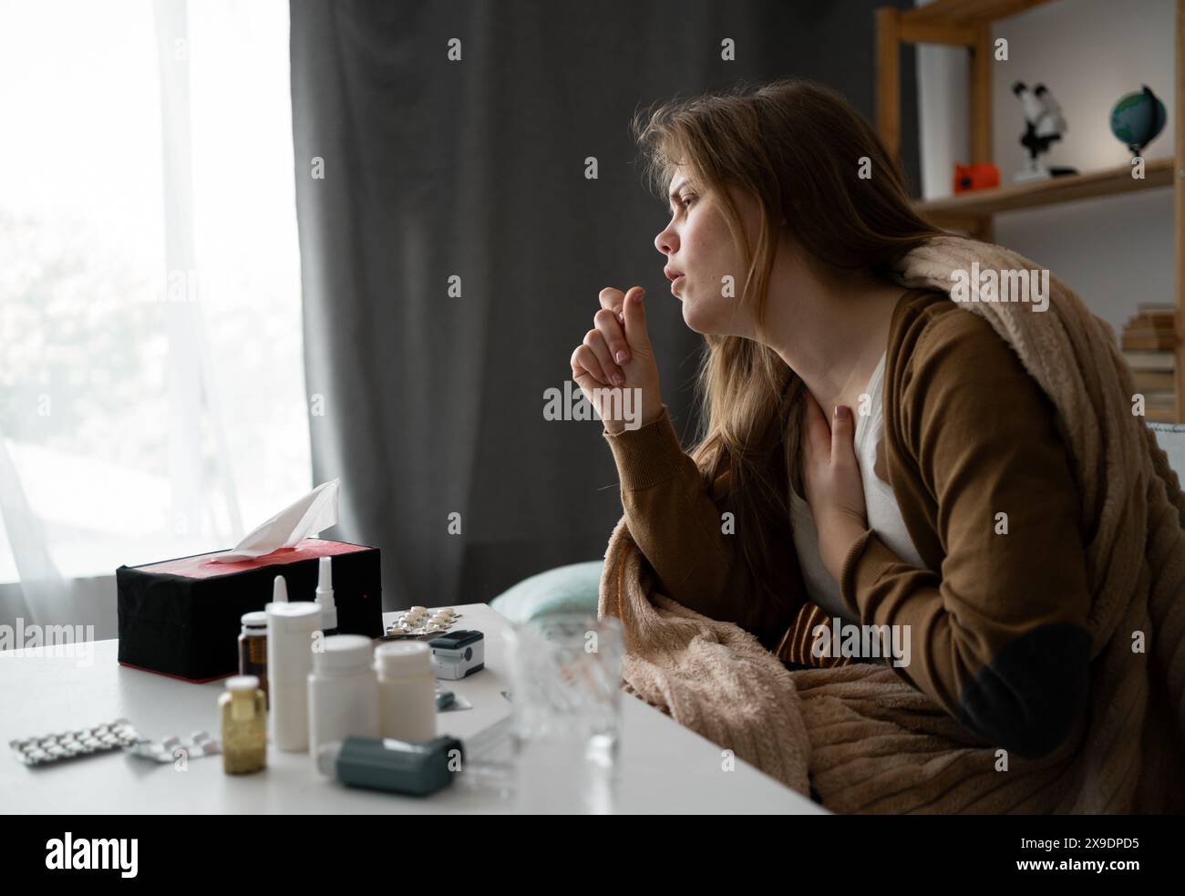 side view. young sick upset woman sitting on the sofa at home covered with a blanket coughing intensely, sick girl with flu symptoms. copy space. bann Stock Photo